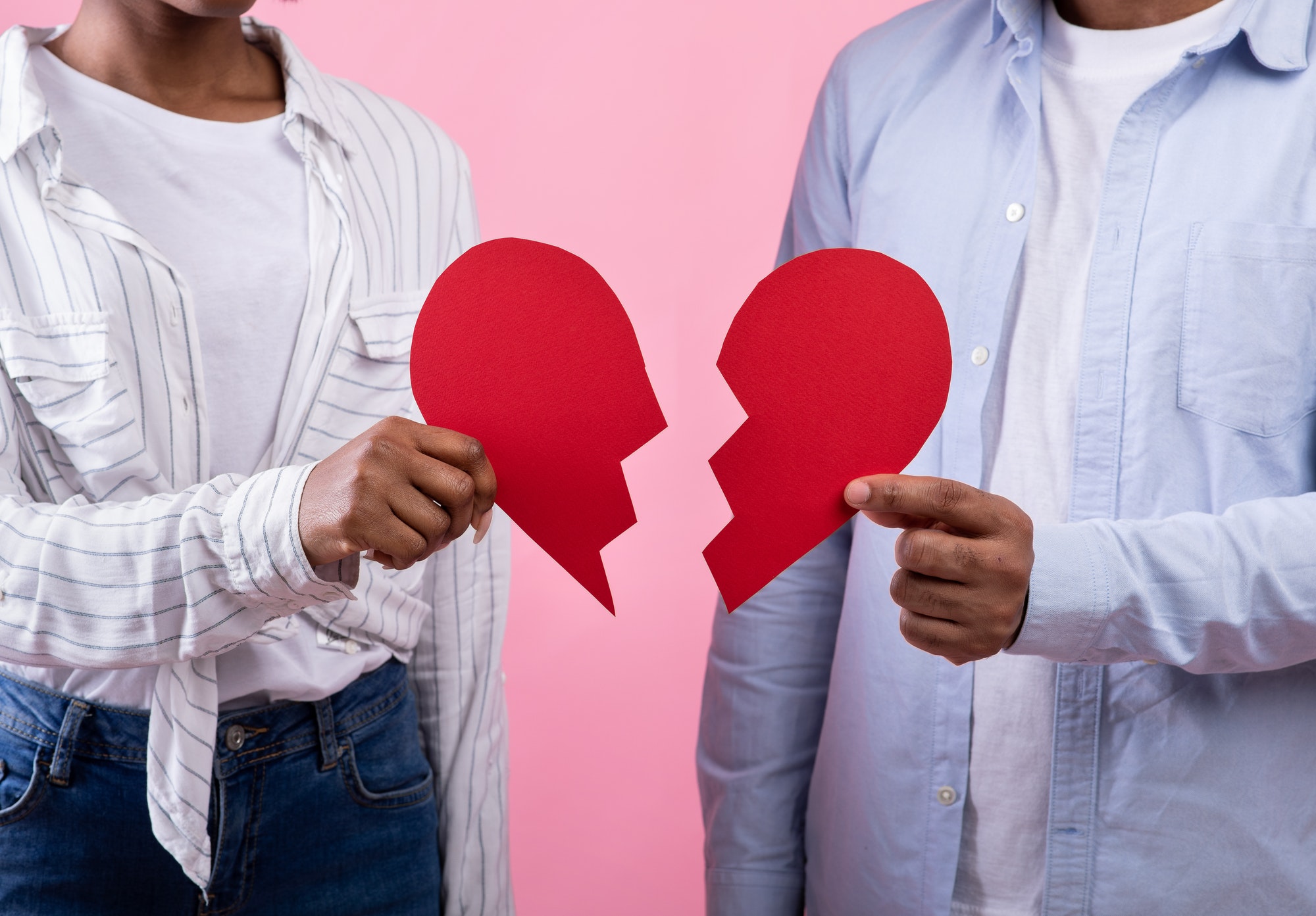 Divorce, separation, quarrel. Unrecognizable black couple holding halves of broken heart over pink